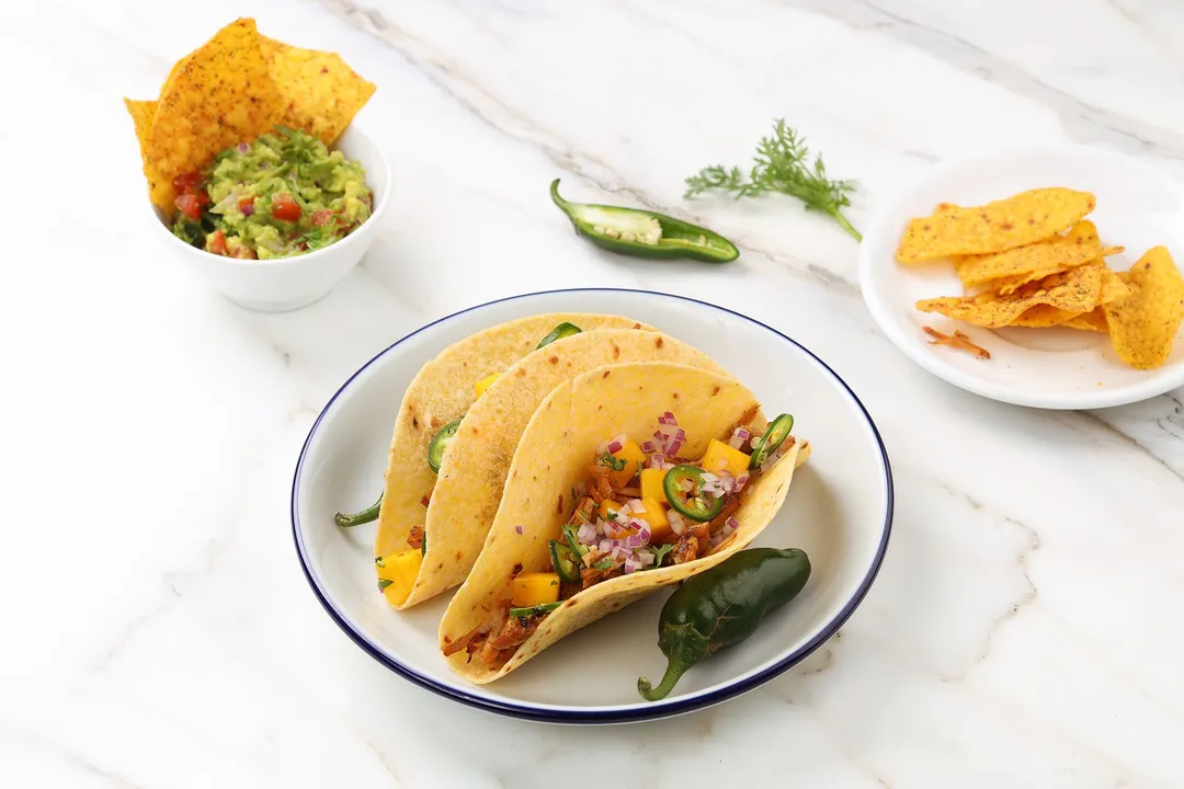 a plate of two tacos next to a plate of tortillas chips and a bowl of salsa