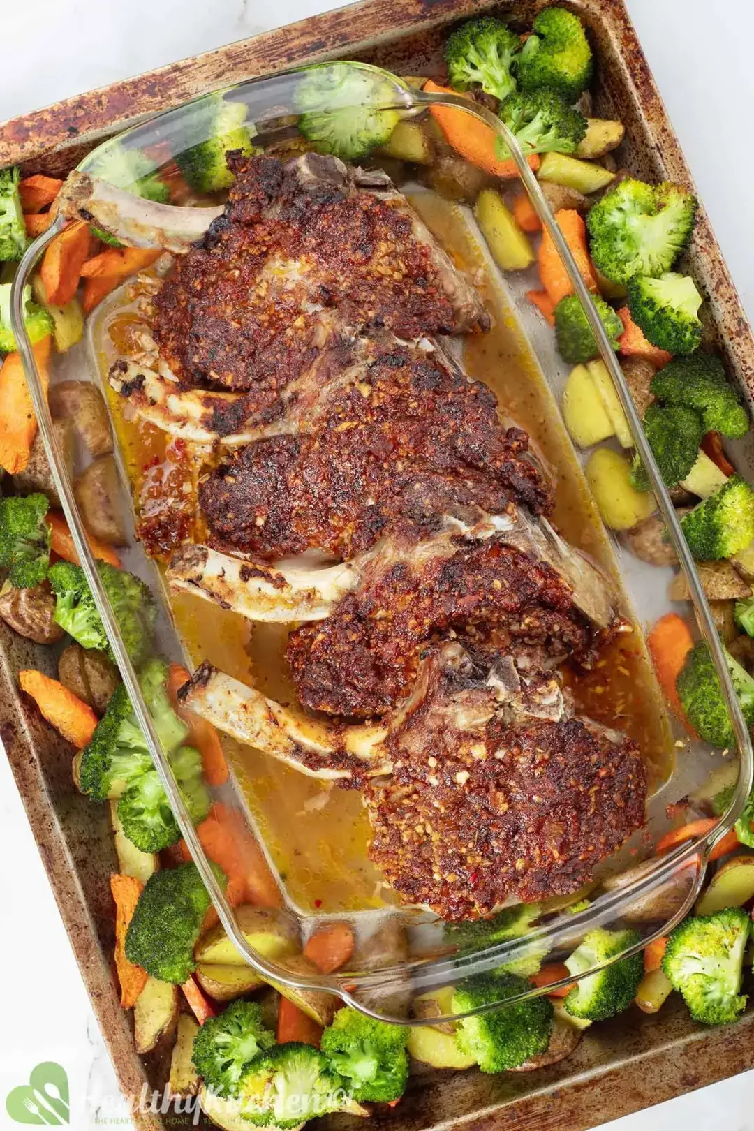 Four golden pork chops in a glass baking dish on a roasted veggie tray