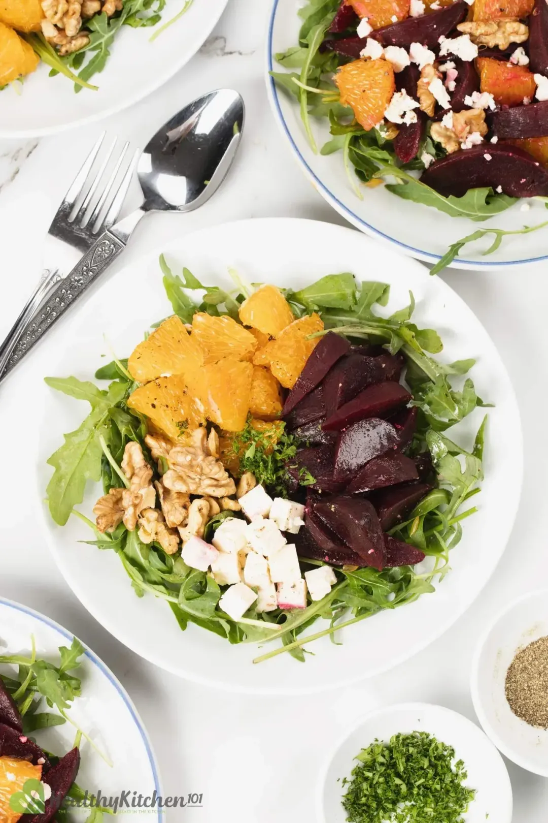 A salad with beets, feta cheese, and greens on white plates with silver cutleries.