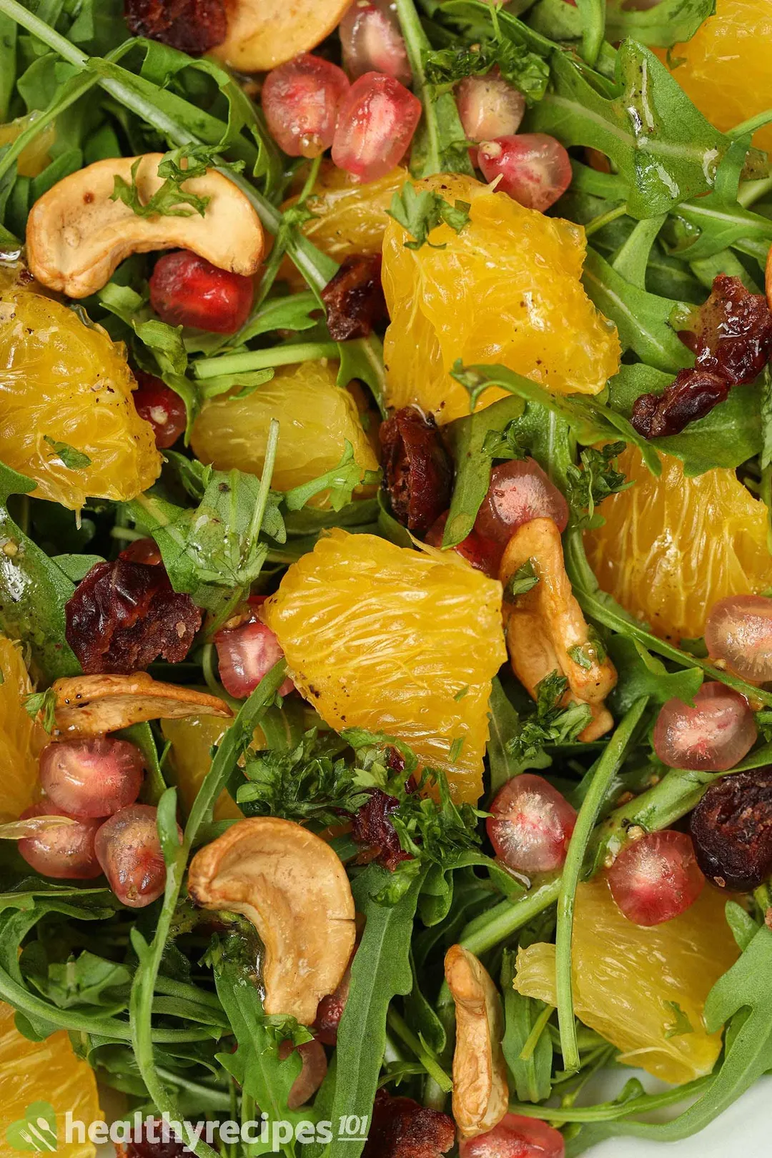 A close-up shot of arugula salad, including orange segments, pomegranate seeds, arugular, and cashews.
