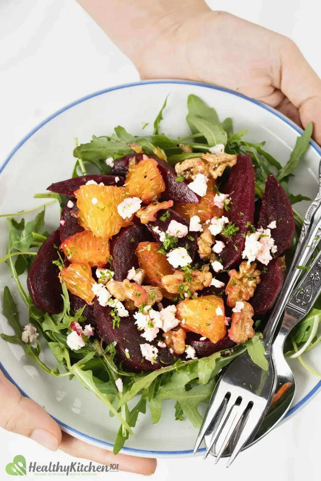 A close-up of a beet and feta cheese salad with greens, orange, and walnuts.