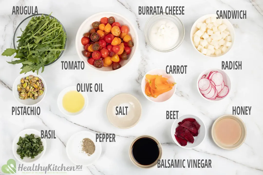 Fresh ingredients for making burrata salad, including burrata cheese, tomatoes, croutons, carrot shavings, and arugula.