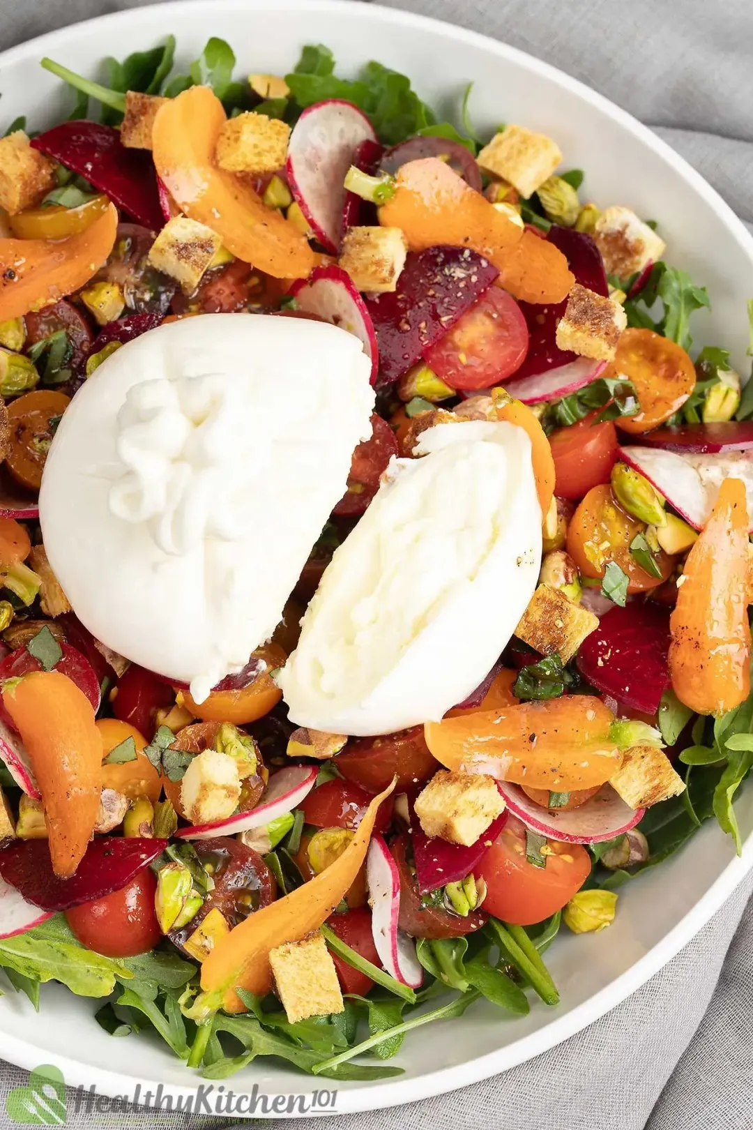 A plate of Burrata salad with fresh greens, cherry tomatoes, and a burrata cheese ball in the middle