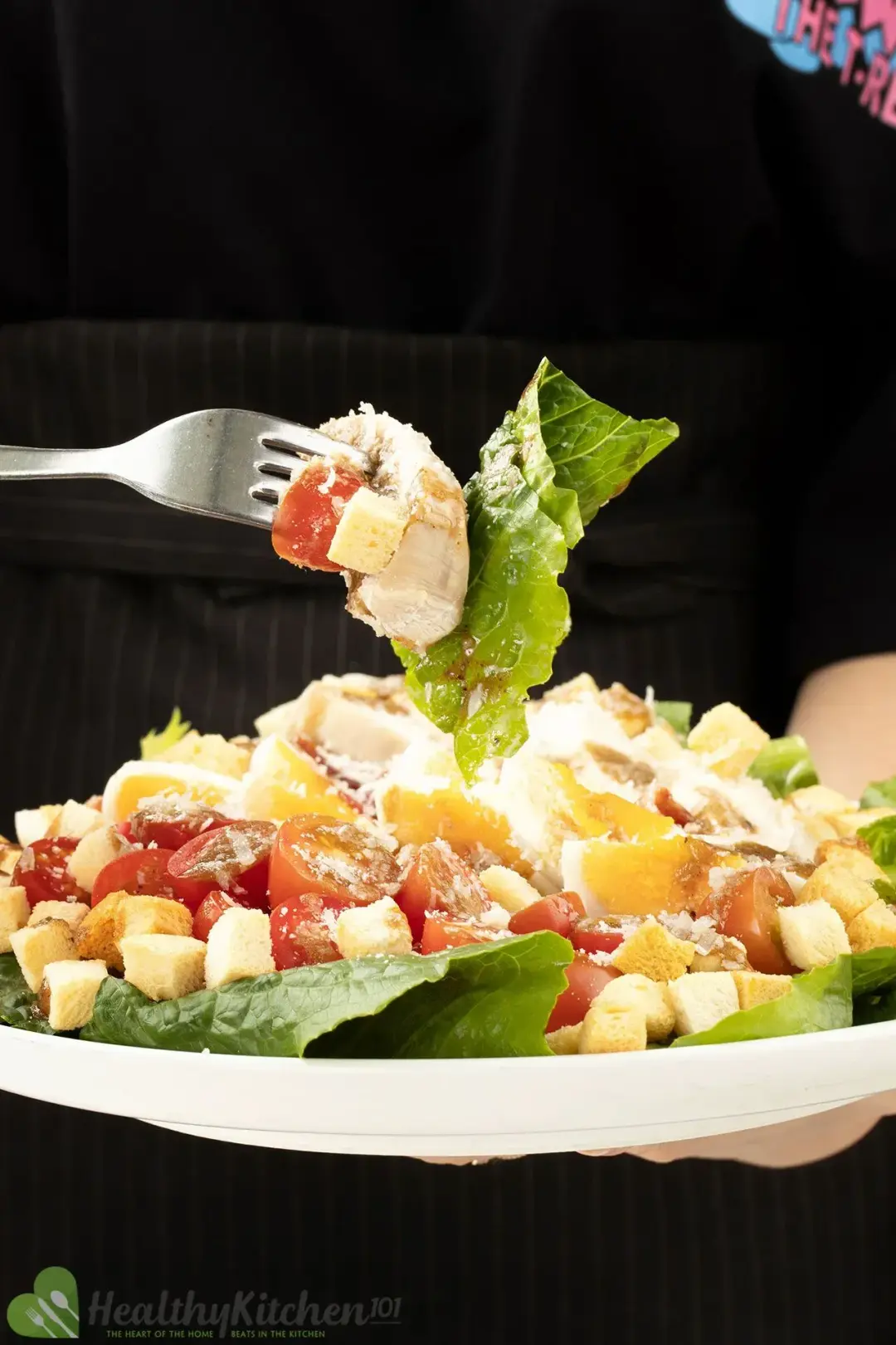 A plate of Caesar salad with lettuce, croutons, eggs, cherry tomatoes, and dressing