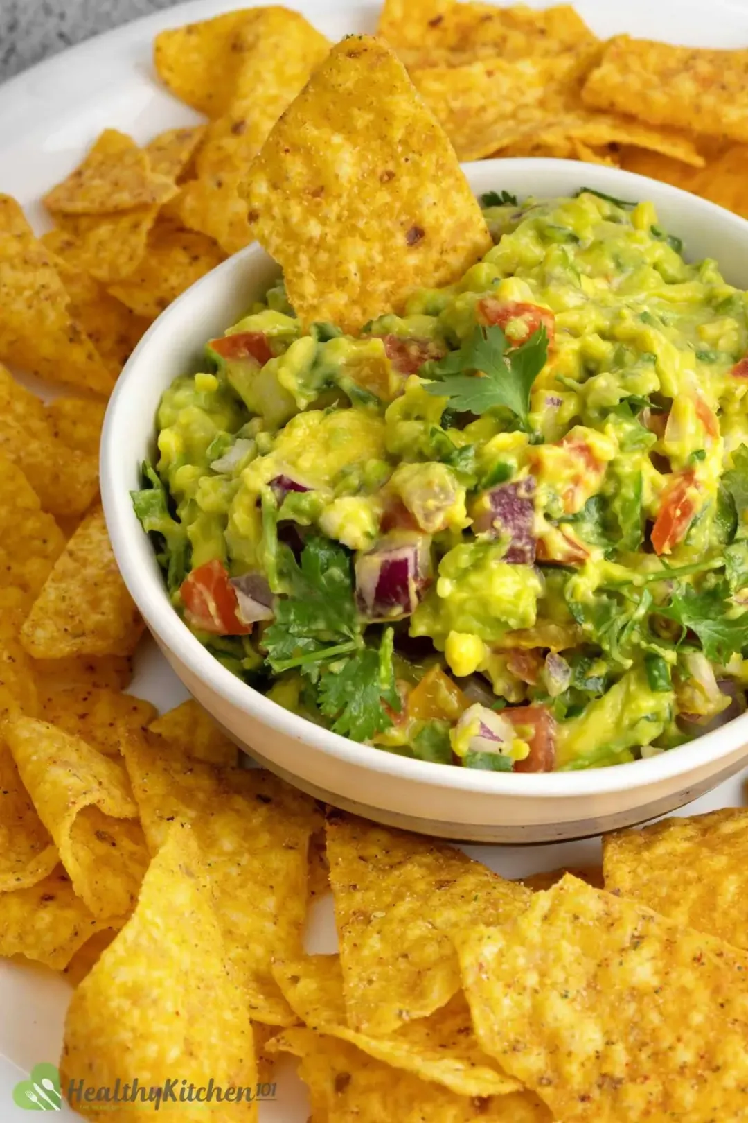 A bowl of guacamole surrounded by chips on a white plate