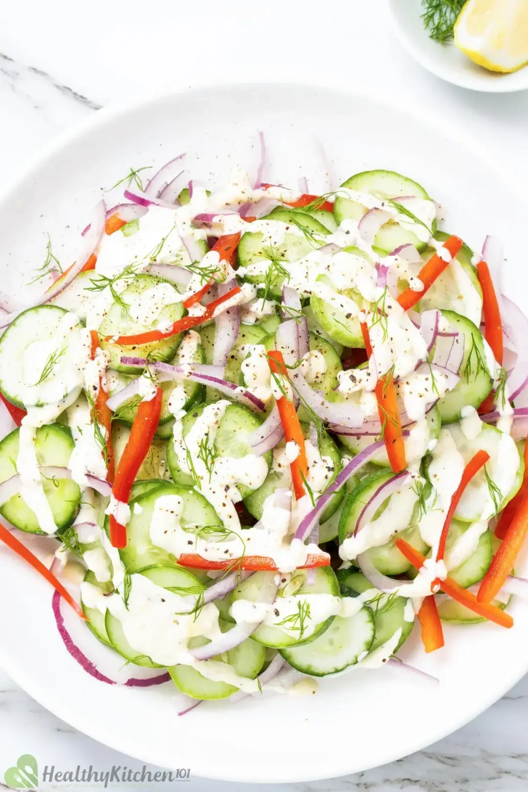 A salad of sliced cucumber, red pepper, dill, red onion, and a white dressing drizzled on top
