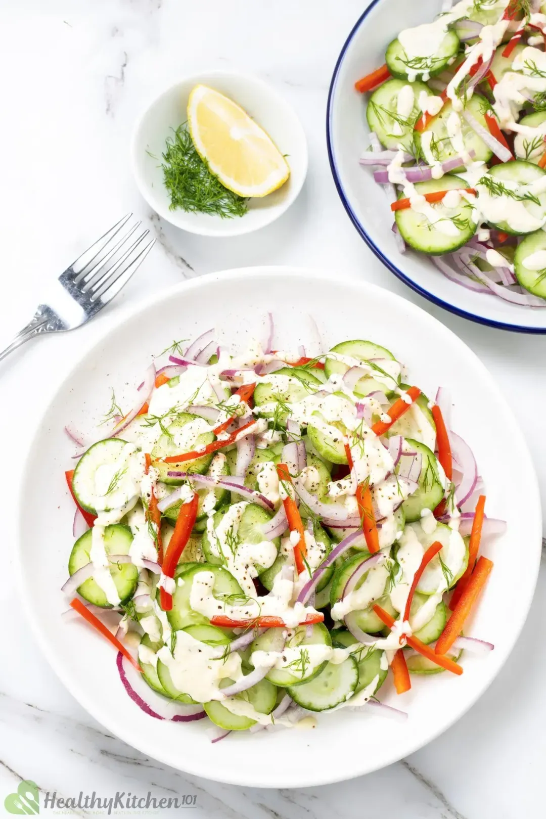 Healthy cucumber salad on two plates with sliced cucumbers, sliced red peppers, red onions, and a light dressing.