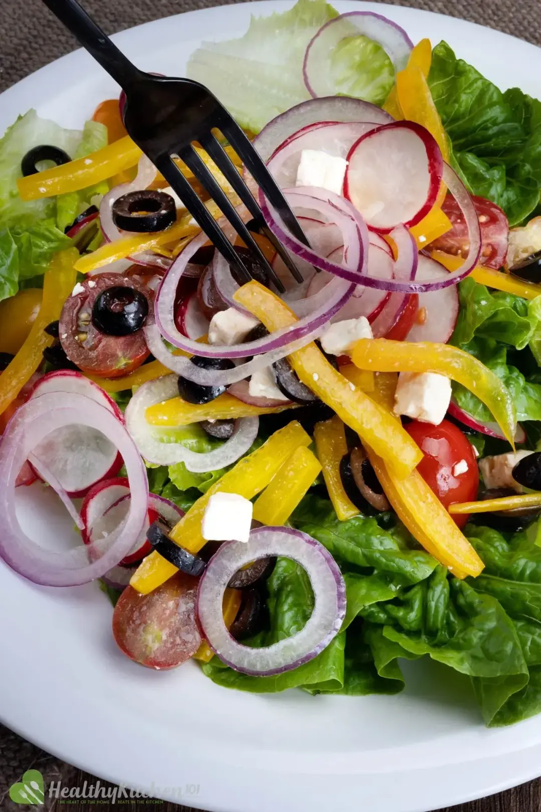 A fork dunked into a dish of Greek salad, full of vegetables of different colors