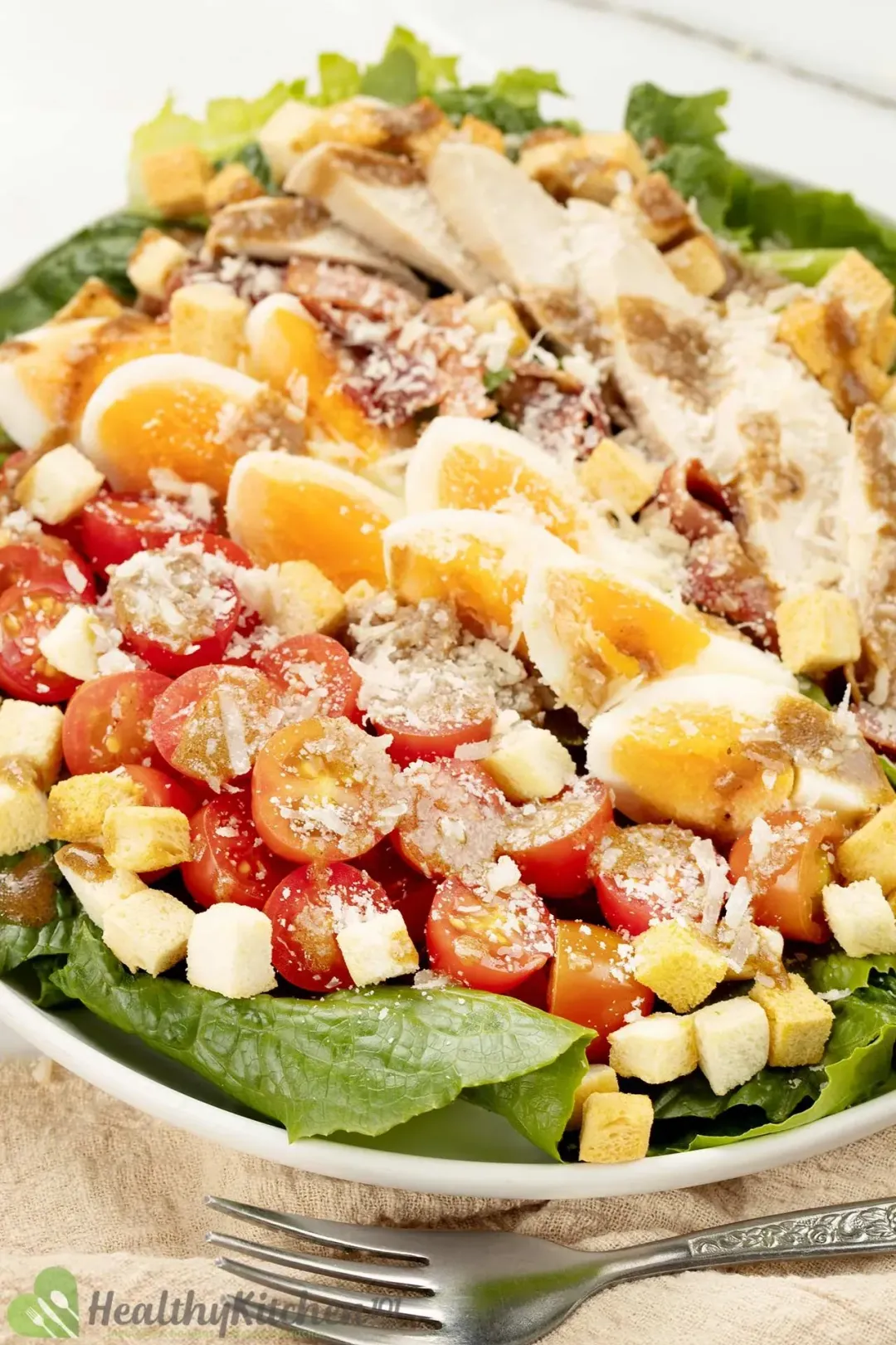 A bowl of homemade Caesar salad with lettuce, croutons, parmesan cheese, eggs, cherry tomatoes, and dressing