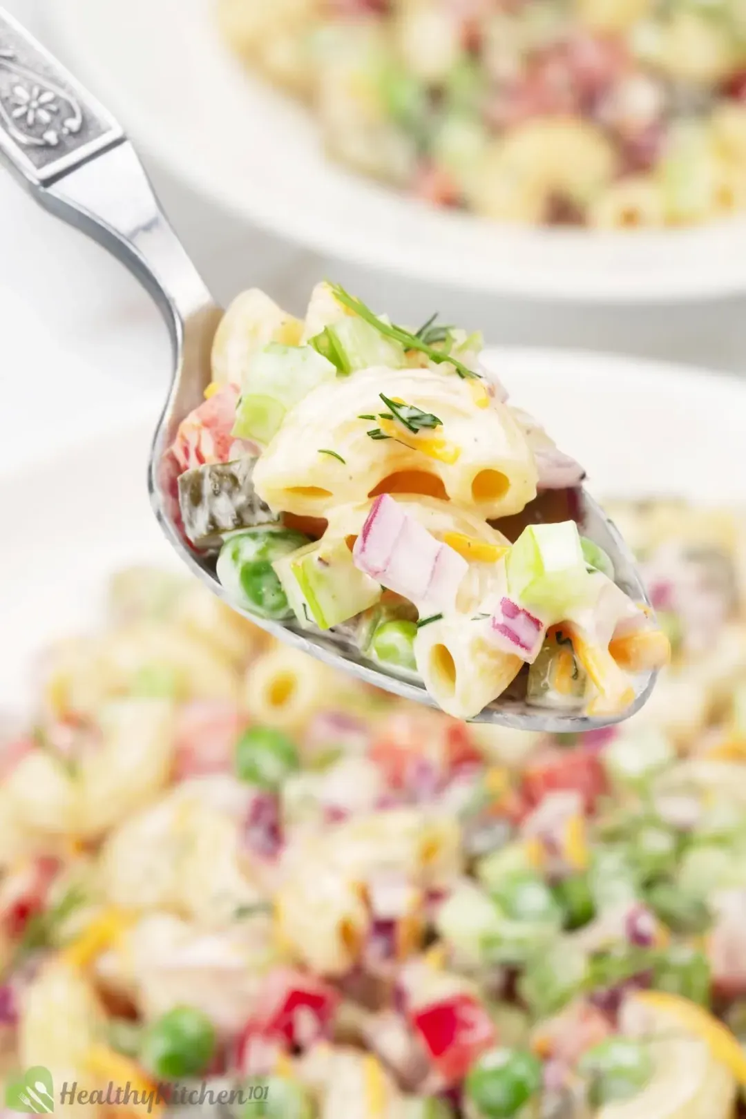 A spoon of macaroni salad with peas and red onion pieces in creamy dressing