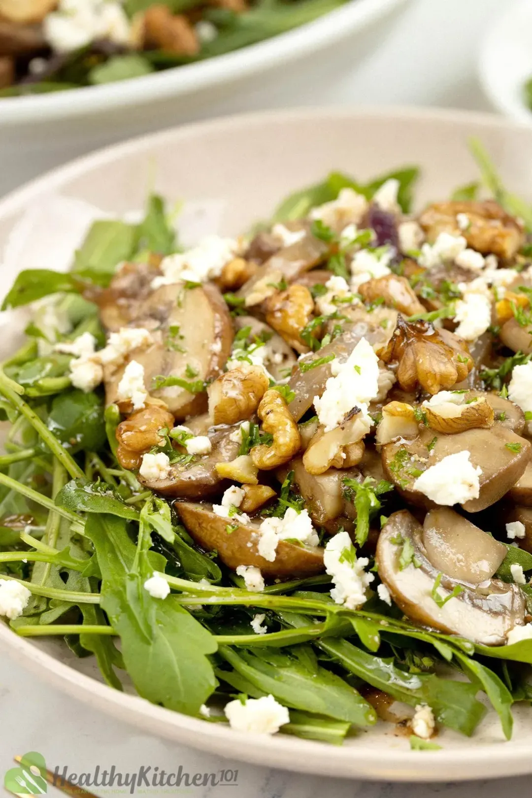 A bowl of mushroom salad with sliced mushrooms, walnuts, cheese, and dressing on top.