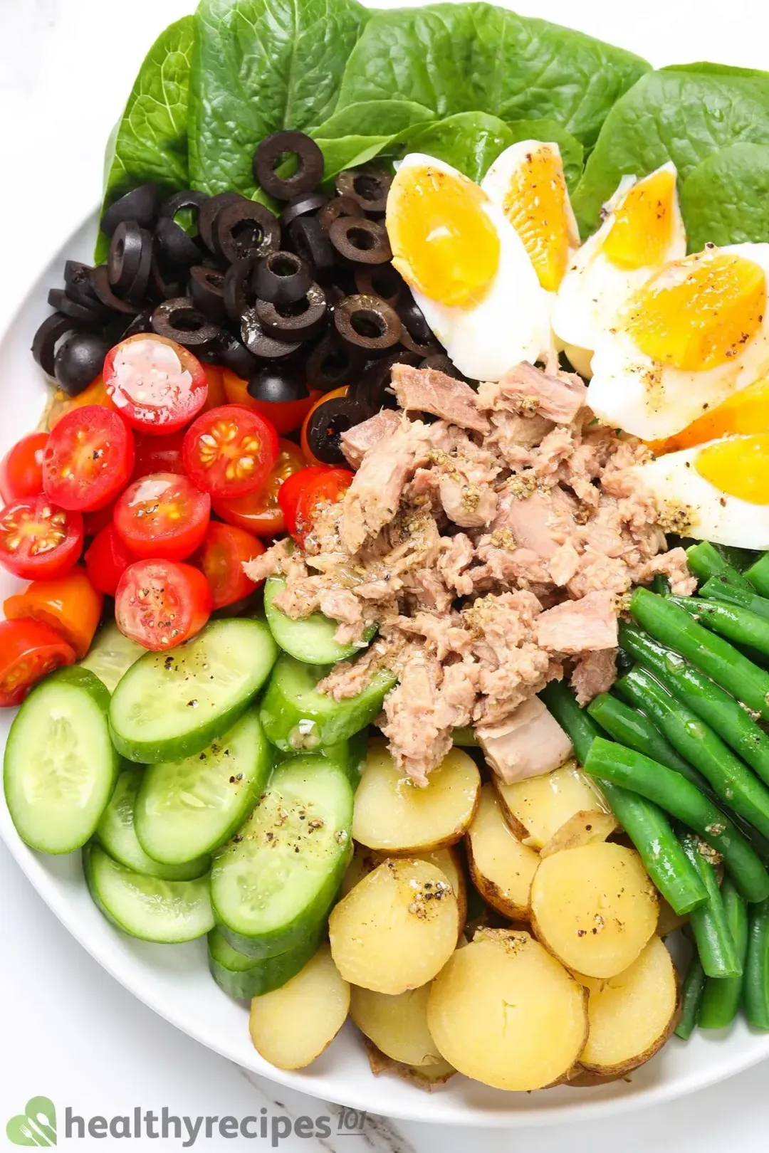 A homemade Nicoise salad with tuna, boiled eggs, olives, green beans, tomatoes, and potatoes on a white plate.