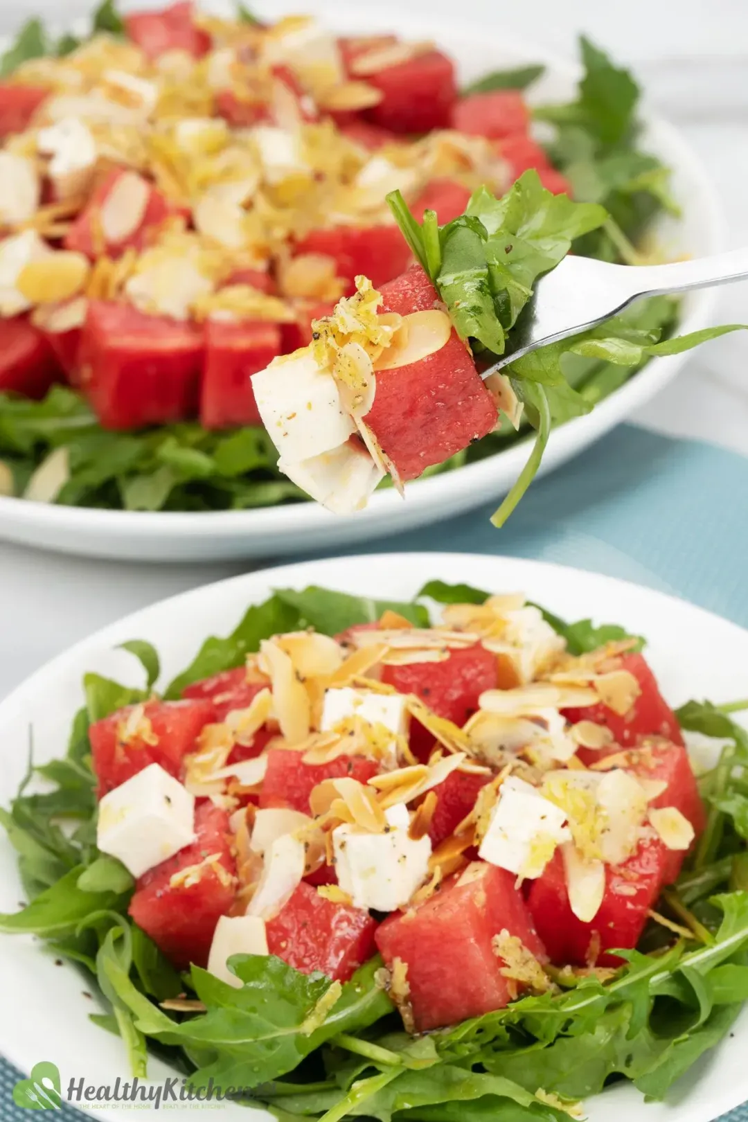 Two plates of watermelon arugula salad, topped with cubed feta cheese and shaved almonds