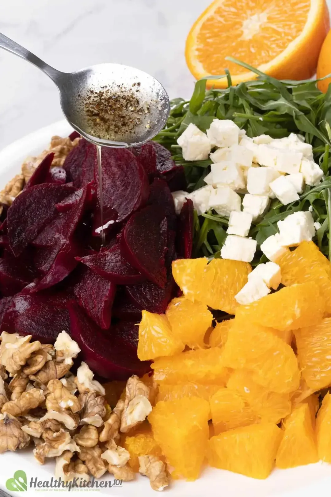 A plate of sliced beetroot, orange, feta cubes, walnuts, and arugula