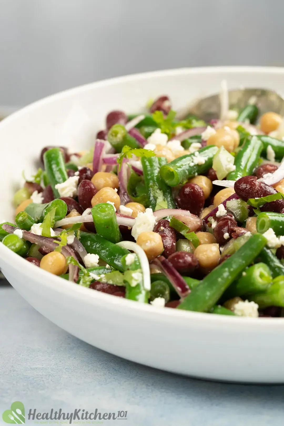 A plate filled with three-bean salad, garnished with red onion slices, cheese, and herbs