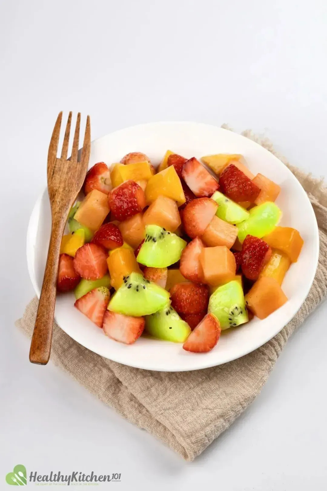 A bowl of fruit salad with strawberries, blueberries, kiwi, and mango on a white background.