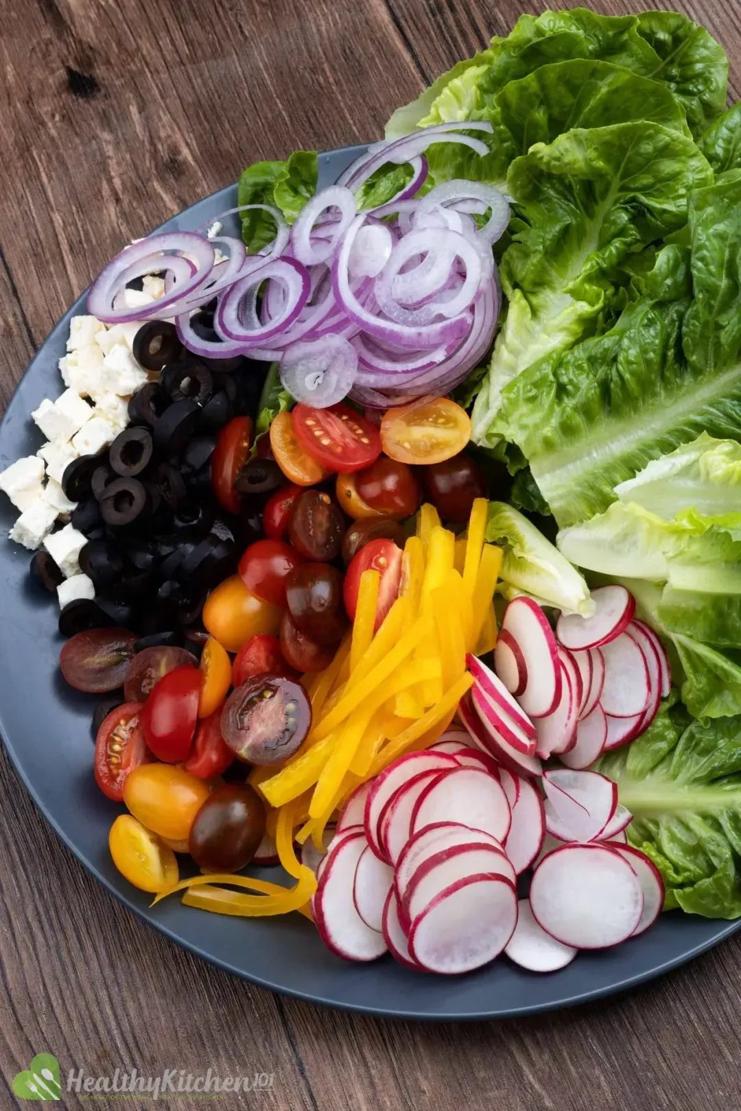 A large plate holding halved cherry tomatoes, sliced yellow peppers, slice radish, lettuce, olives, cubed feta, and lettuce
