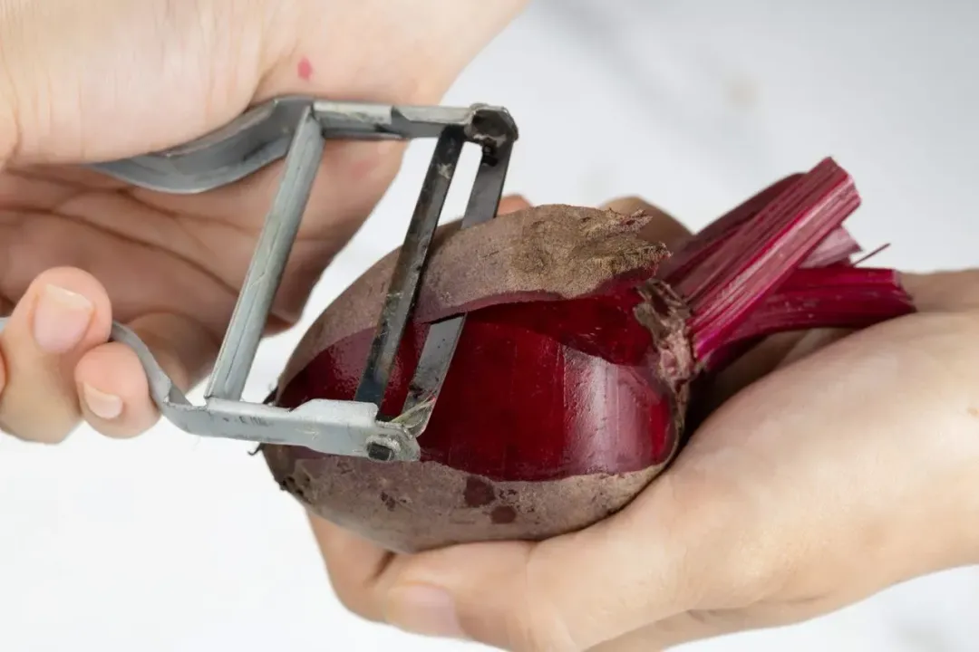 Two hands peeling a beetroot with a peeler