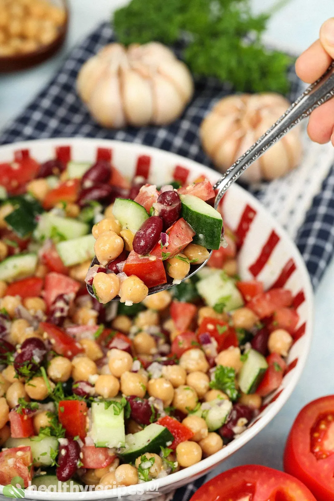 A spoon scooping up chickpeas, diced cucumber, diced tomatoes, and kidney beans from a bowl of vegan chickpea salad.