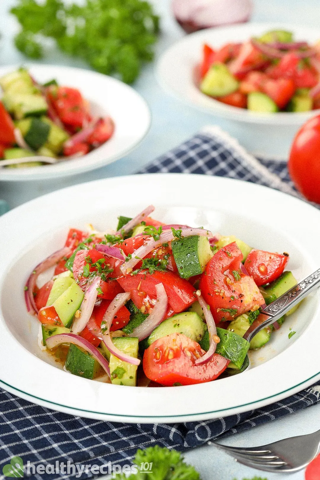 Plates of cucumber tomato salad, consisting of pieces of tomato, cucumber, red onion, and chopped parsley