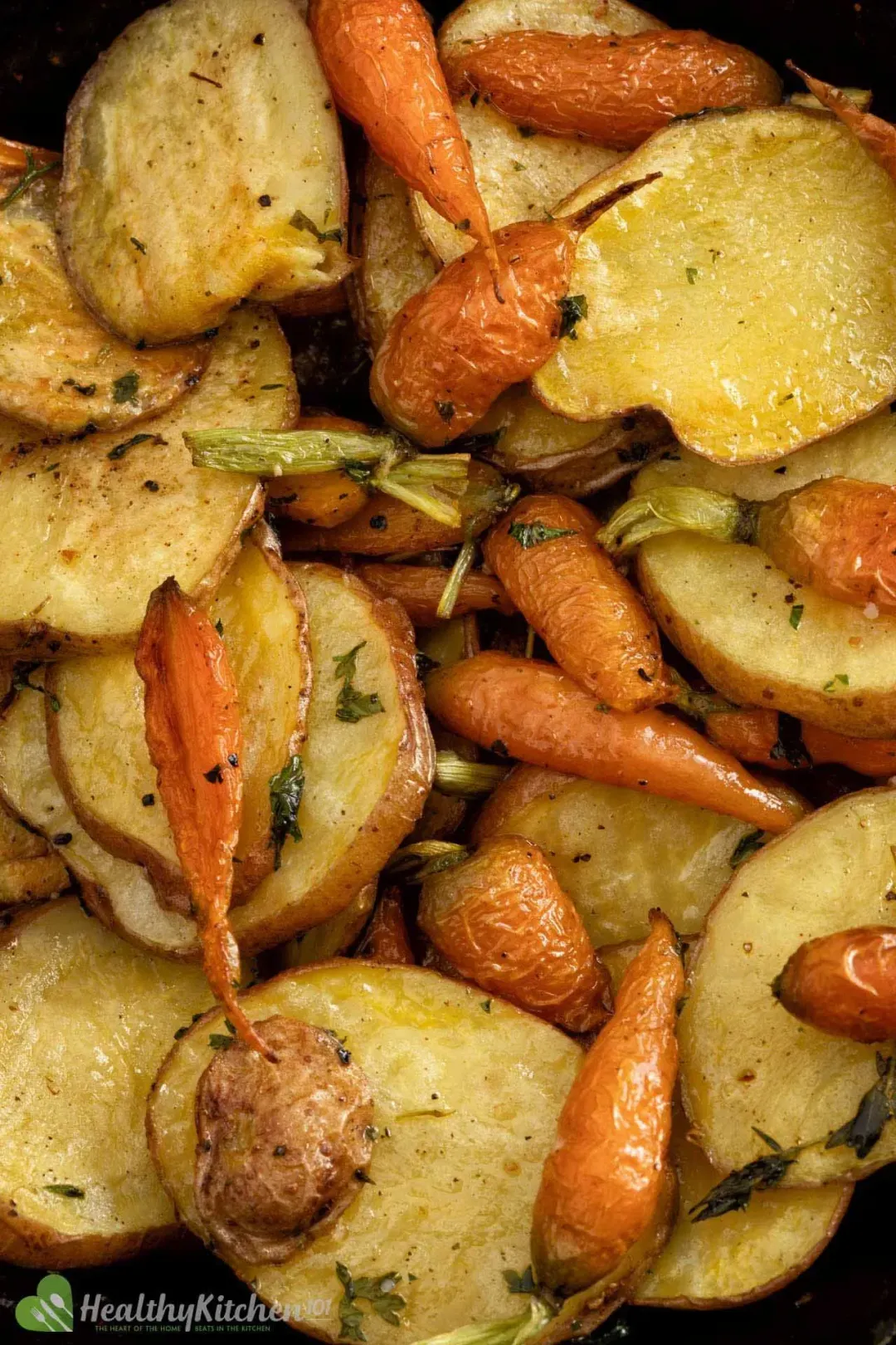 A close-up shot of baked potato slices and baby carrots, glistening with oil