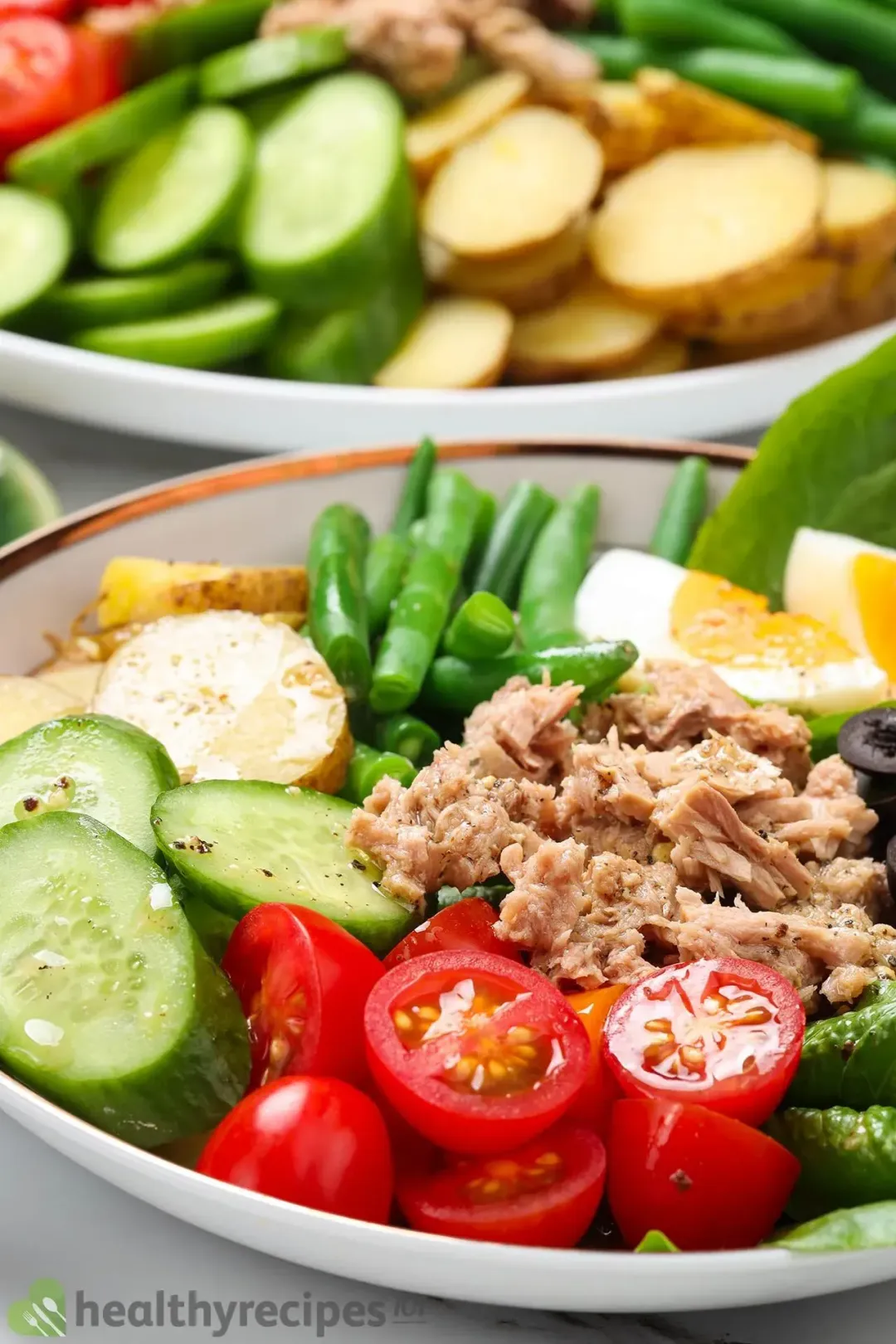 A bowl of Nicoise salad with boiled eggs, green beans, cherry tomatoes, olives, and tuna on a bed of lettuce.