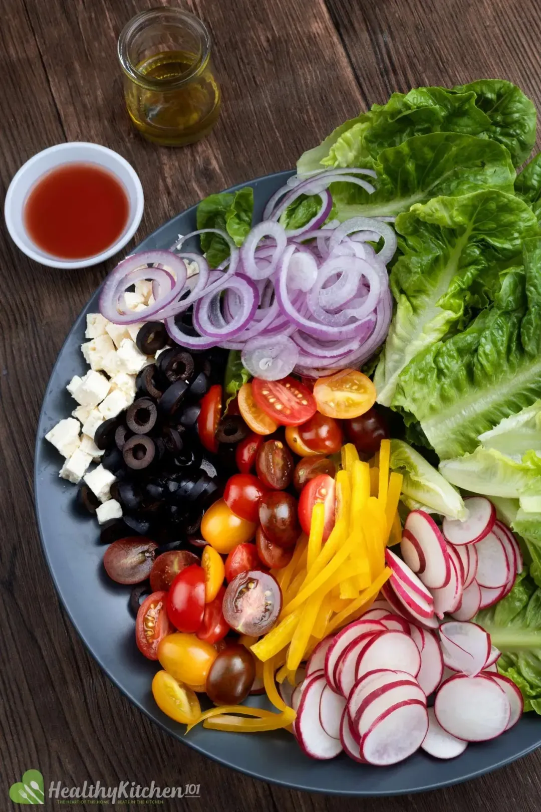 A large plate holding halved cherry tomatoes, sliced yellow peppers, slice radish, lettuce, olives, cubed feta, and lettuce