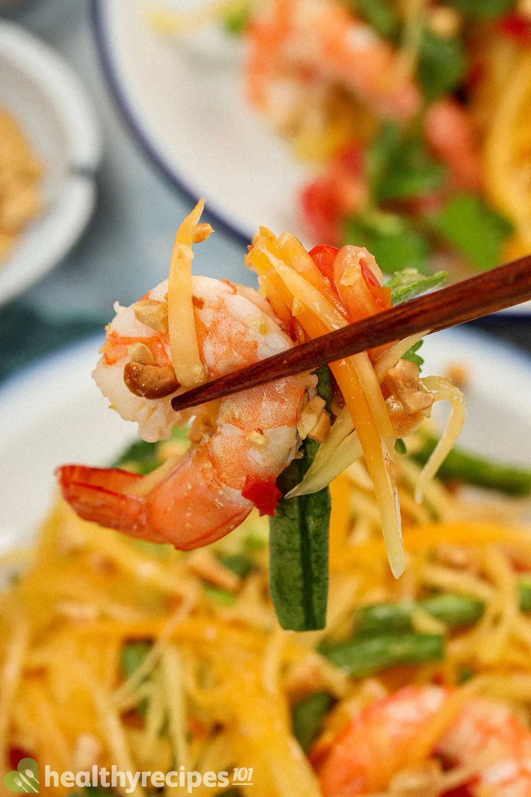 Chopsticks picking up pieces of a papaya salad, including cooked shrimp, shredded papaya, and long beans