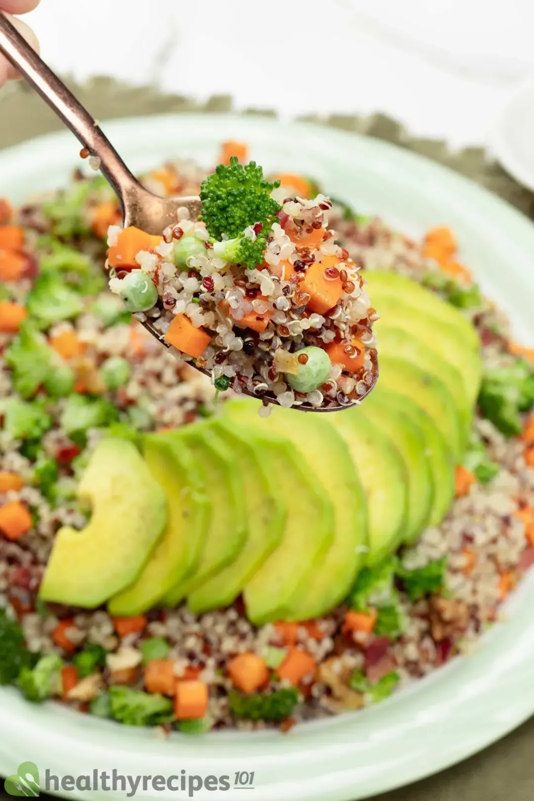A spoon full of colorful quinoa salad hovering over a plate of quinoa and avocado salad.