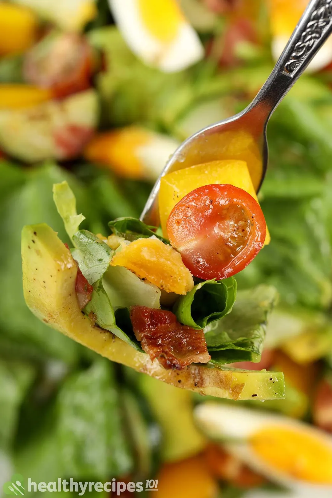 A fork piercing through a slice of avocado, chopped bacon, a piece of lettuce, a diced piece of bell peppers, and half a cherry tomato