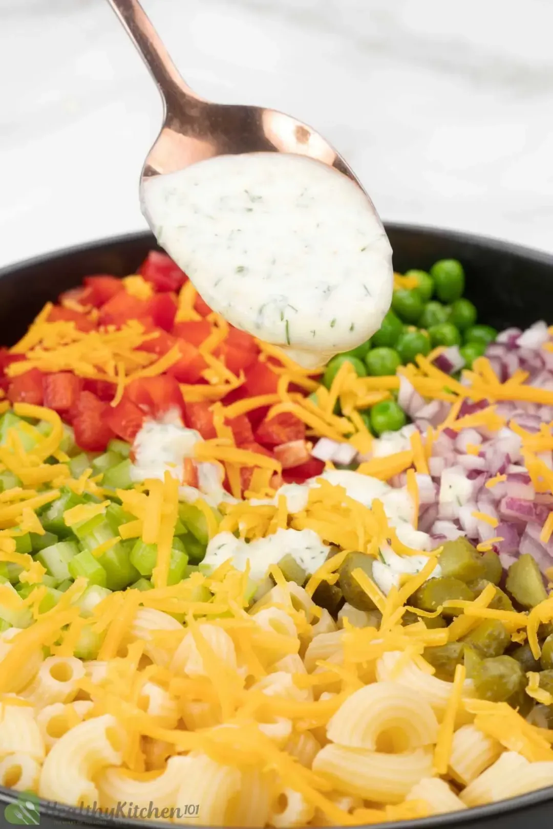 A bowl of macaroni salad with a creamy dressing, diced vegetables, and herbs on top.