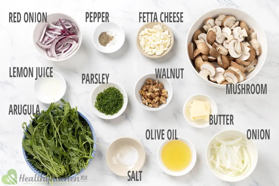 A photo of various ingredients including mushrooms, arugula, walnuts, cheese, and dressing ingredients on a white background.