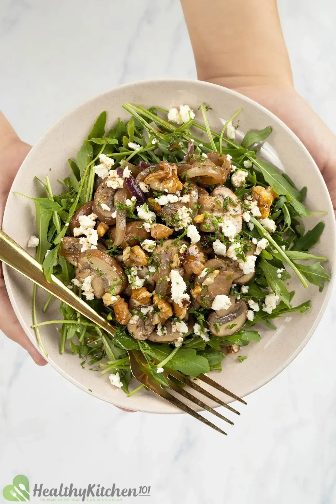 A salad with mushrooms, feta crumbles, walnuts and arugula on a plate.