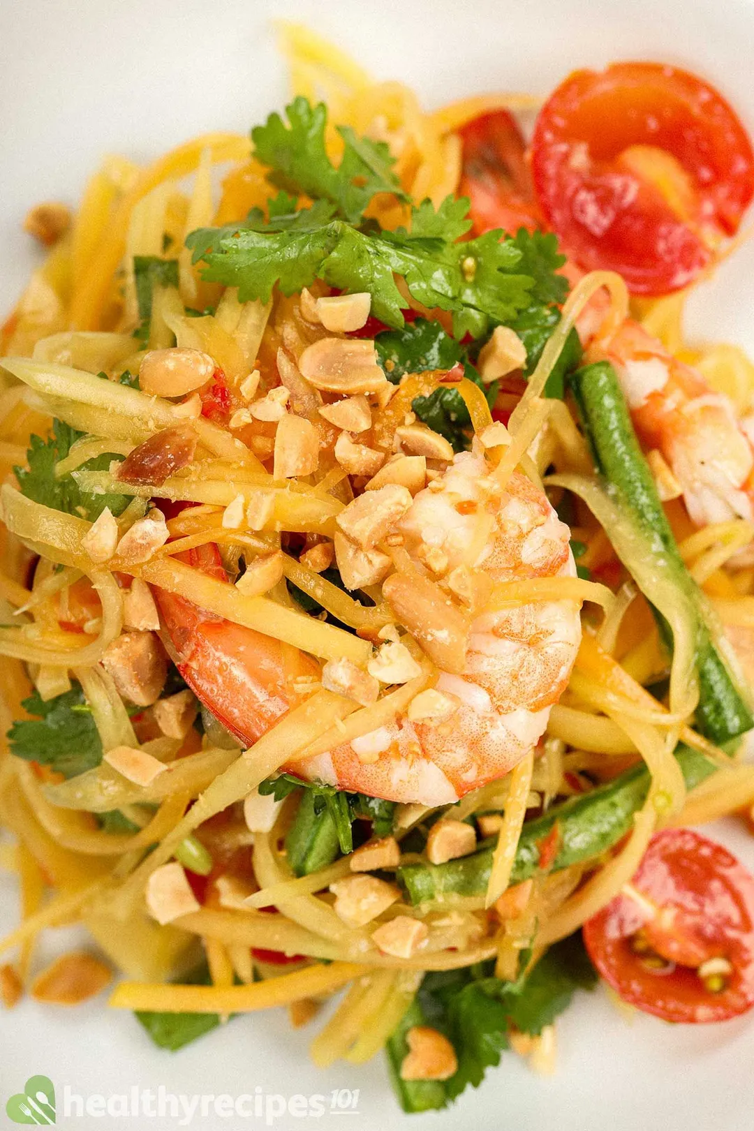 A close-up shot of a papaya salad, including cooked shrimp, shredded papaya, halved tomatoes, and roasted peanuts