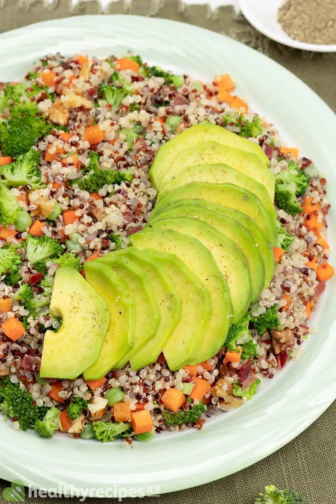 A colorful quinoa salad with sliced avocados on top.
