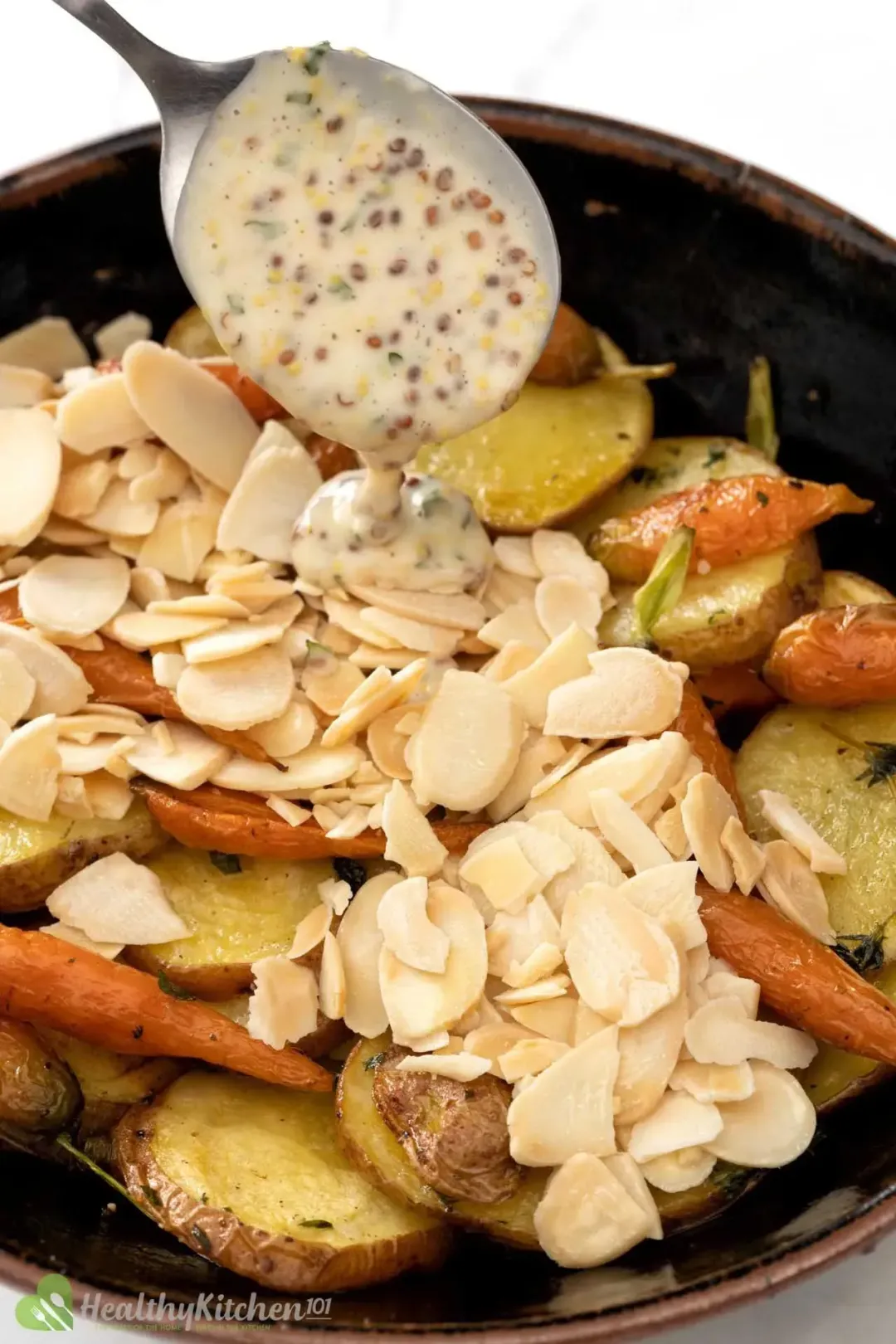 A bowl of mustard potato salad with sliced potatoes, baby carrots, and shaved almonds, spooned with mustard dressing on top