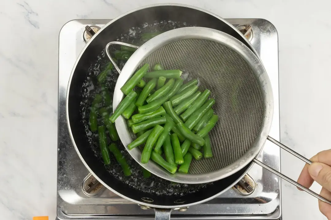 Green beans blanching in a sieve over a pot for three bean salad