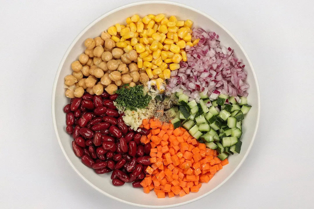 bean, chickpea, corn, diced cucumber, diced carrot, diced onion in a plate