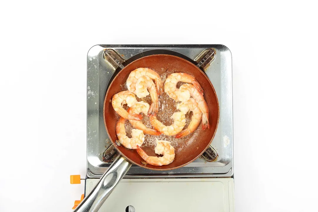 A small pan cooking shrimp on a portable gas stove