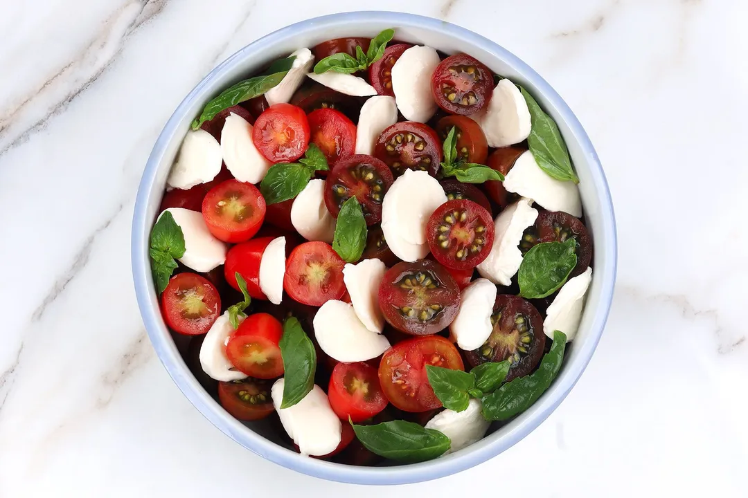 half tomatoes, basil leaves and mozzarella cheese in a bowl