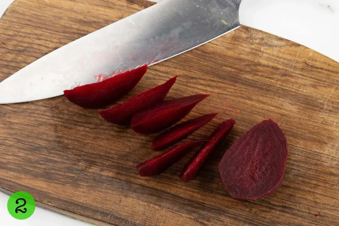 Beets in a colander being cut on a wooden board