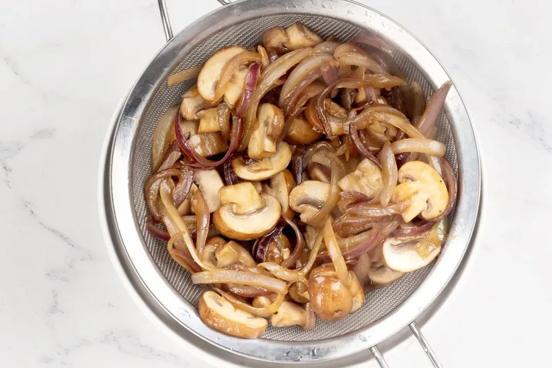 Saueed mushrooms and onions inside a metal sieve