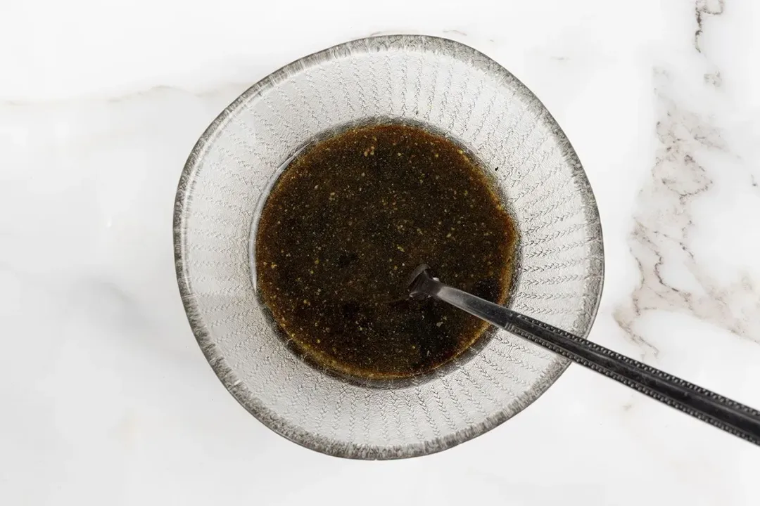 A mixing bowl with a red salad dressing with a spoon dunked in