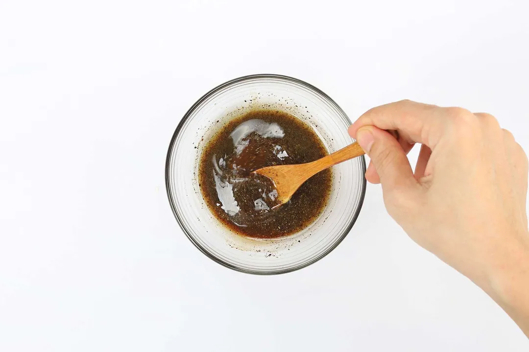 a wooden spoon stirring dressing in glass bowl 