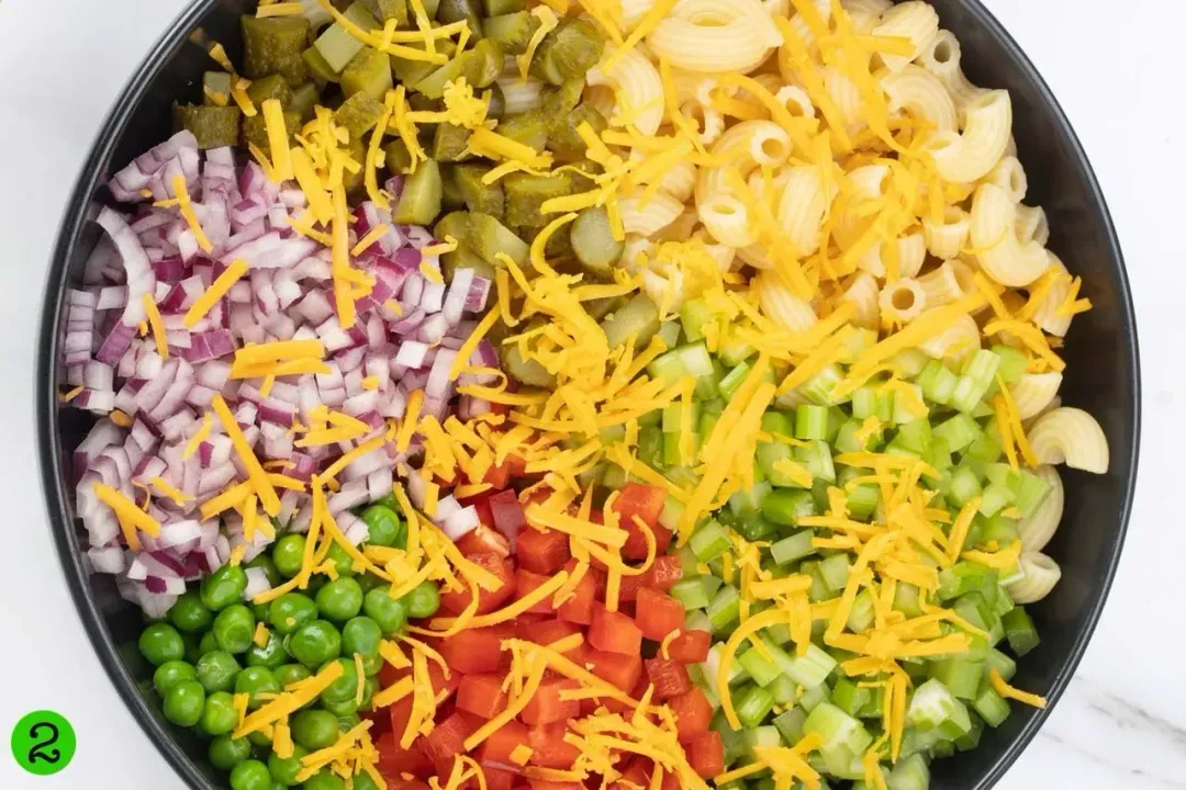 A bowl of macaroni salad mixed with vegetables on a wooden surface.