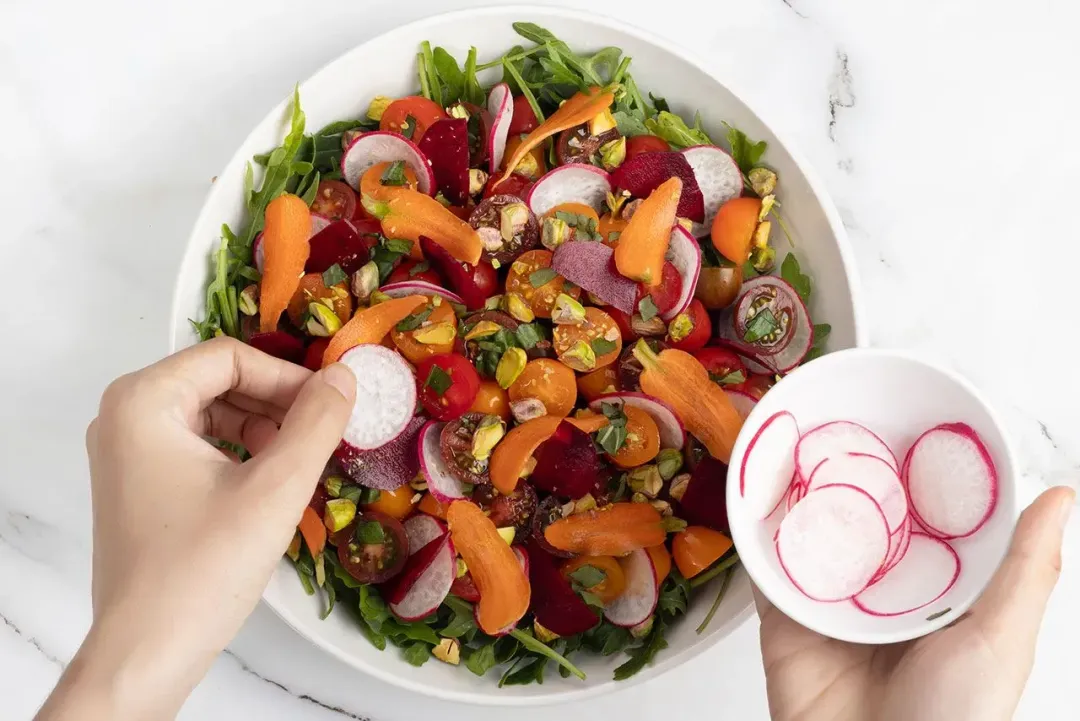 A salad with burrata cheese, tomatoes, arugula, croutons, and radish slices arranged on a plate.
