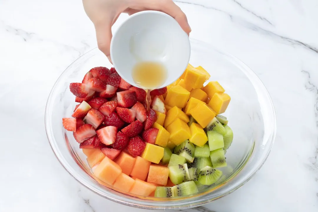 pouring dressing from small bowl to a big bow of fruit