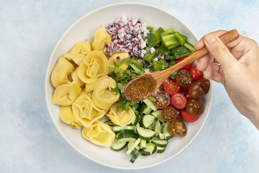 a wooden spoon pouring dressing on top of salad plate