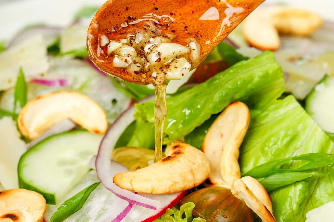 a wooden spoon pouring dressing to a plate of salad