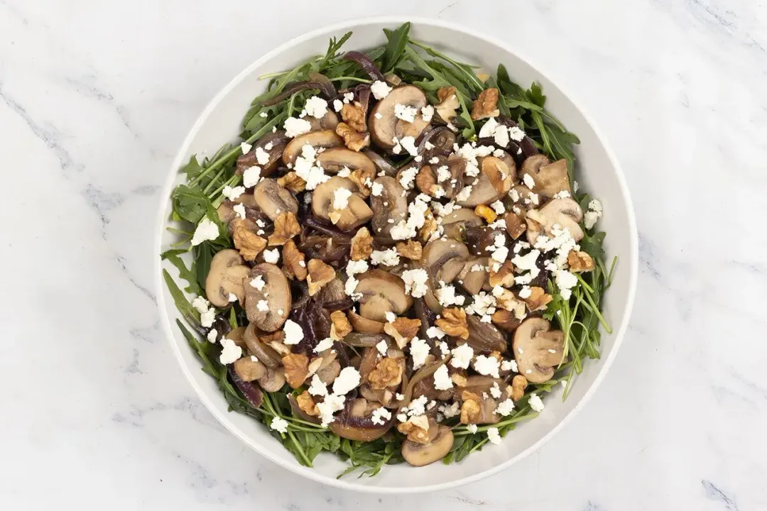 A close-up of the mushroom salad, showing the mushrooms, arugula, onions, walnuts, and feta cheese crumbles